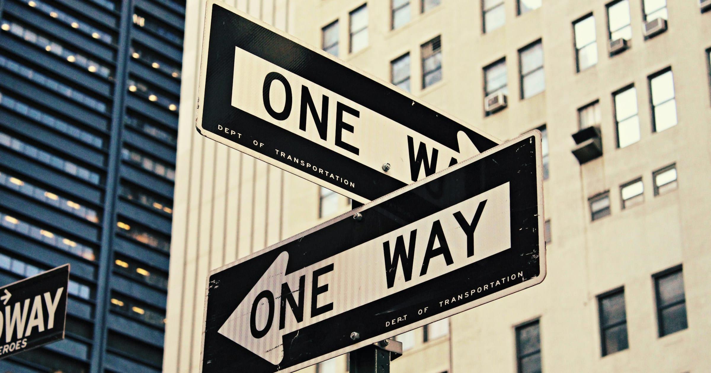 Two one-way street signs on the same pole, pointing in opposite directions