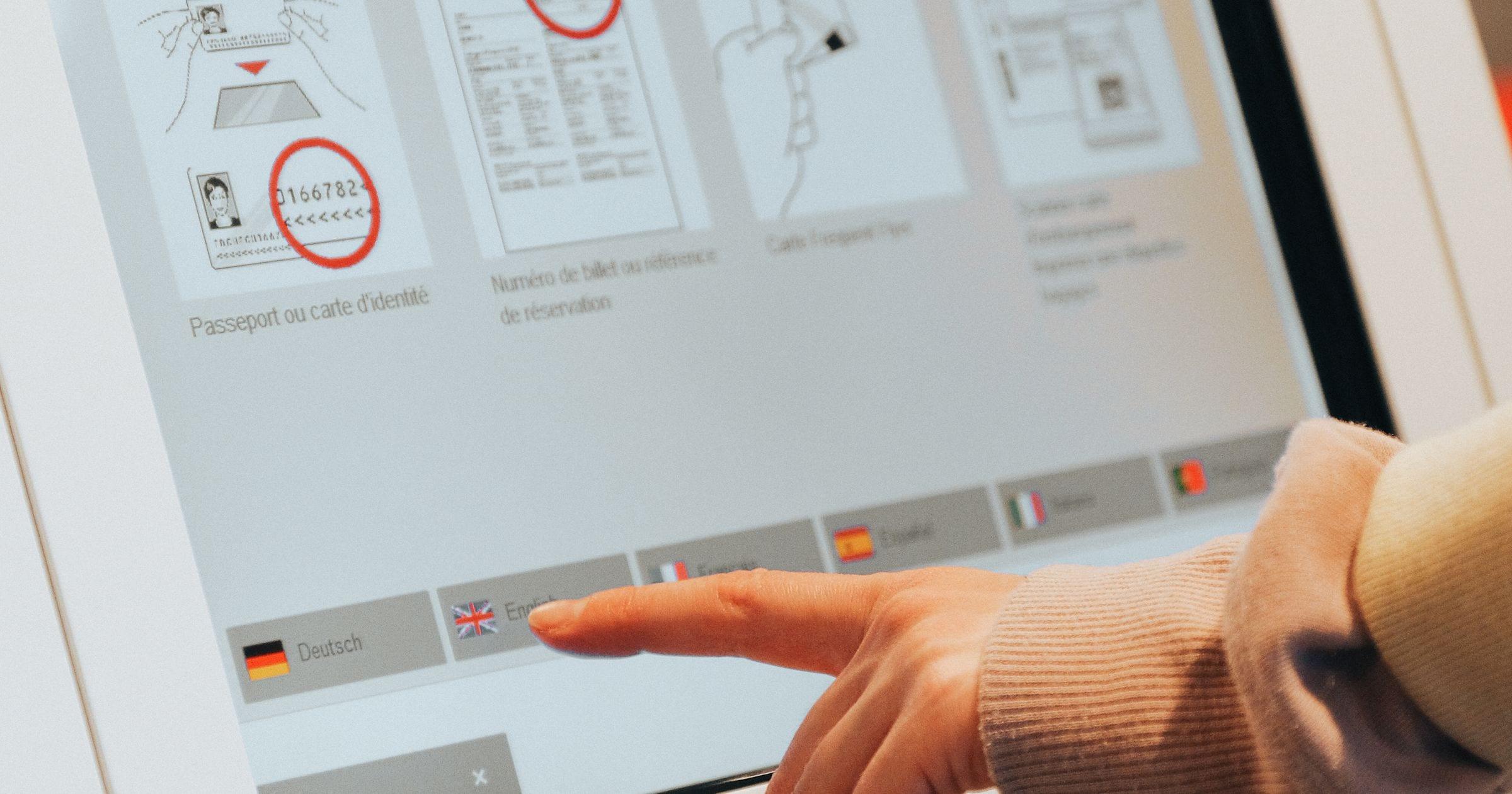 A hand using a self-service check-in kiosk at an airport